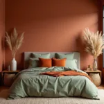 A bedroom with sage green bedding and terracotta accent wall