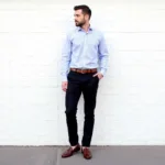 Striped Shirt Black Pants Men's Style: A man showcases a smart casual look with a finely striped blue and white shirt tucked into black pants, completed with brown leather loafers, demonstrating a classic and versatile outfit.